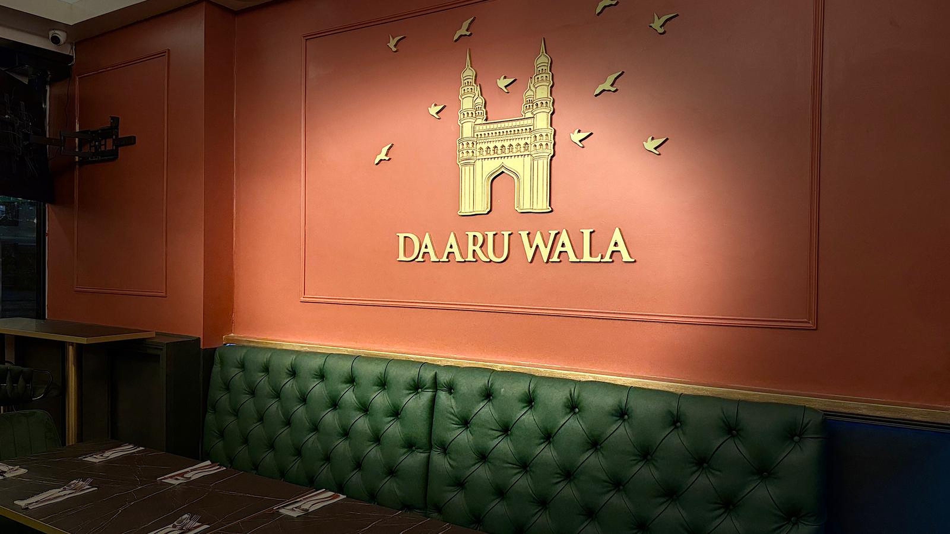 Elegant Charminar Daaru Wala wall logo in gold against our heritage red interior wall